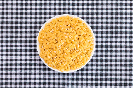 Uncooked Chifferi Rigati Pasta in White Cup on Black Checkered Towel. Fat and Unhealthy Food. Classic Dry Macaroni. Italian Culture and Cuisine. Raw Pasta