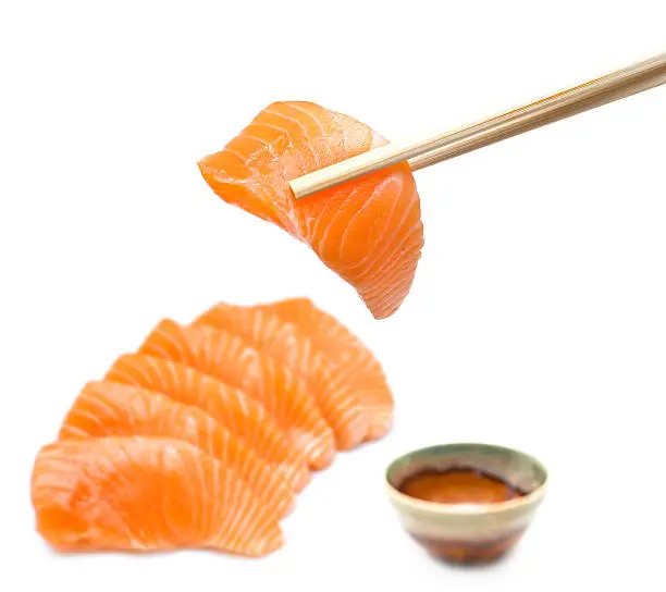 Isolated salmon sashimi set with chopsticks holding a piece of sliced salmon