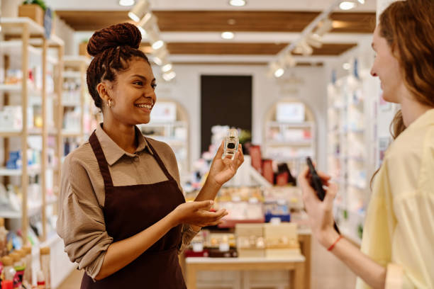 Saleswoman giving consultation to customer in store Young smiling saleswoman giving consultation to customer about perfume in cosmetics store makeup product photography stock pictures, royalty-free photos & images