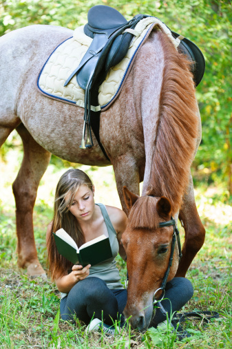 Beautiful young woman reading book with horse, against green of summer park.