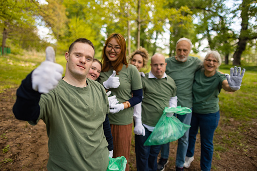 Group of volunteers including people with down syndrome in a wooded area giving a thumbs up for environmental conservation