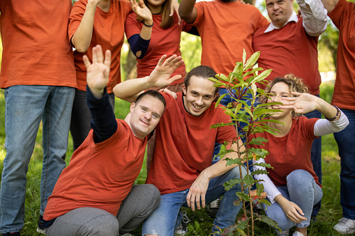 Multiracial group of volunteers waving to camera after planting a tree in a forest