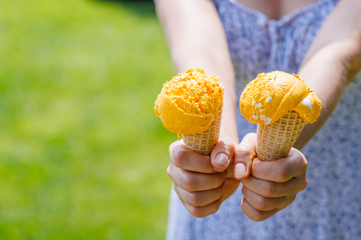 Woman's hands holding refreshing ice cream in waffle cones treats with a hint of zesty lemon flavour. With copy space