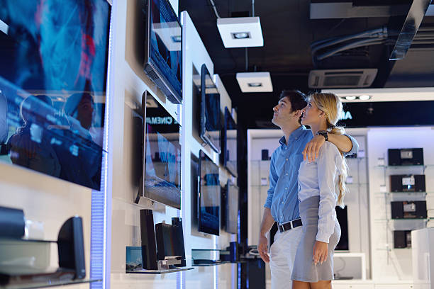 Young couple in consumer electronics store buy tv Young couple in consumer electronics store looking at latest laptop, television and photo camera to buy lcd flat tv electrical equipment stock pictures, royalty-free photos & images