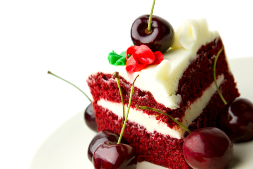 Delicious red velvet layer cake with white frosting garnished with fresh cherries against white background.
