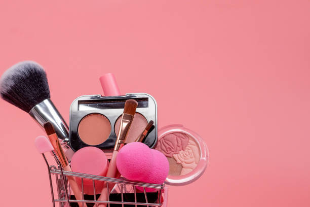 istock Creative concept with shopping trolley with makeup on a pink background. Perfume, sponge, brush, mascara, eye shadow, lip gloss in the basket 1536821301