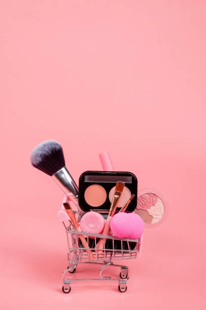 istock Creative concept with shopping trolley with makeup on a pink background. Perfume, sponge, brush, mascara, eye shadow, lip gloss in the basket 1536821456