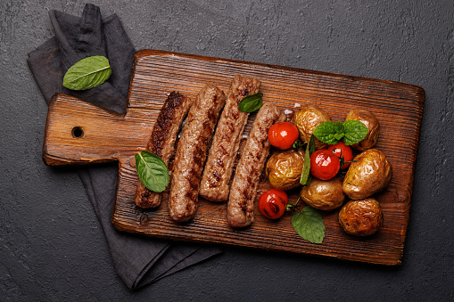 Delicious grilled sausages and potatoes on a wooden board. Flat lay
