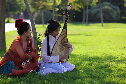 Young ladies under tree relaxing and playing a Mandarin Instrument