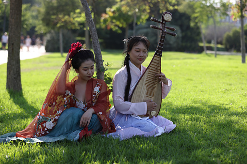 Young ladies under tree relaxing and playing a Mandarin Instrument