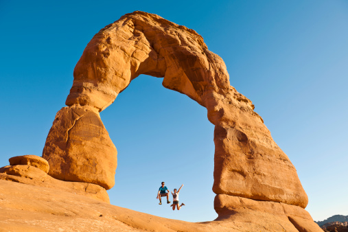 Happy young couple jumping, Delicate Arch, Utah, USA.