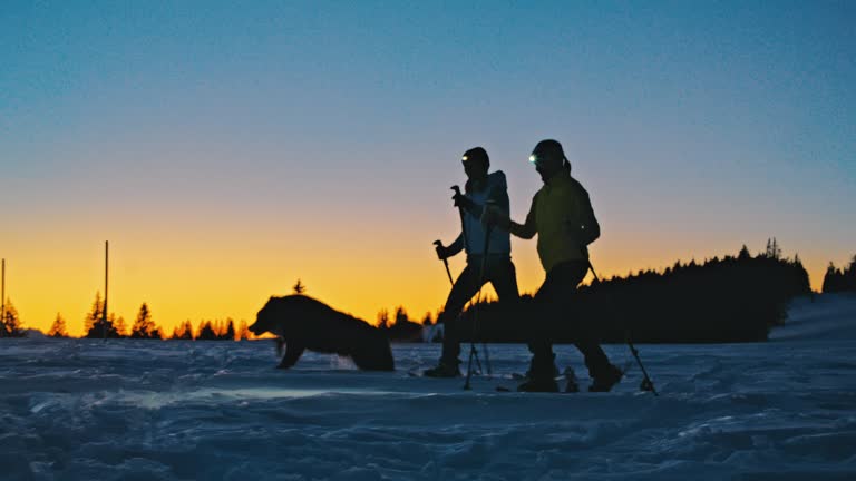 SLO MO Two women snowshoeing over snow in winter countryside with their dog