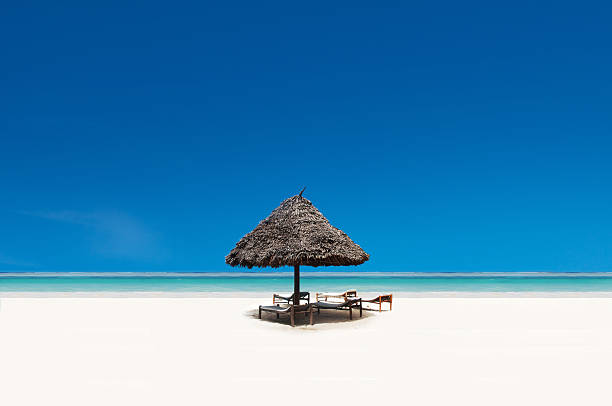 Beach paradise Straw hut on an idyllic beach with blue sky backdrop and white sand indo pacific ocean stock pictures, royalty-free photos & images
