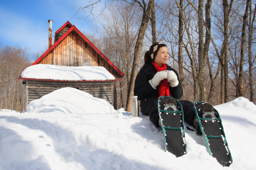 Snowshoeing in winter. Woman on snowshoes resting from hiking in beautiful winter forest. Cabin in the background. From Quebec, Canada. For more