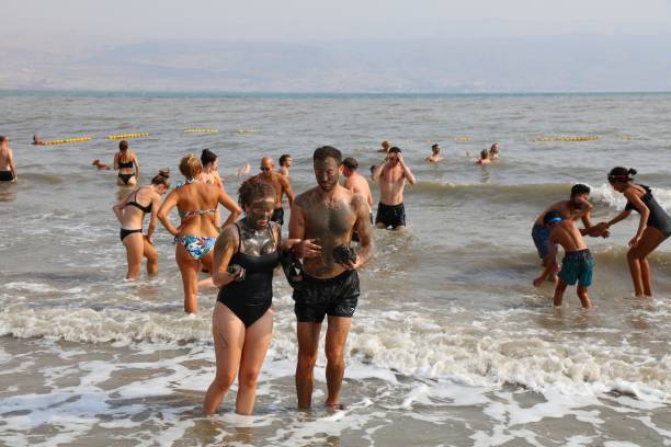 Tourists visit Dead Sea beach in Israel. Dead Sea is the lowest point on Earth, with famous dark mud believed to have therapeutic properties.