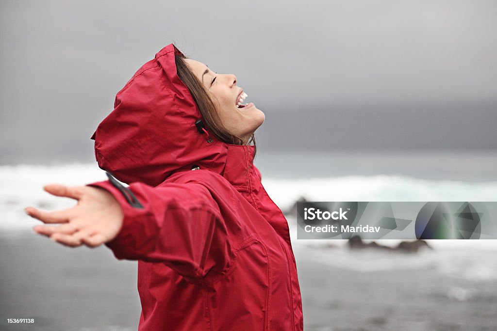 A woman in a red rain poncho enjoying the rain Rain. xwoman enjoying a grey rainy fall day on the beach. Young smiling xwoman in red raincoat. Click for more: Beach Stock Photo