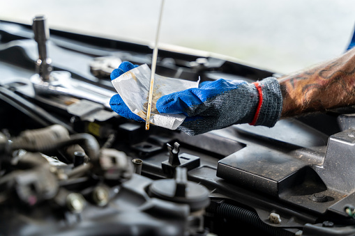 Close up hands of a male car mechanic checking car oil with engine in background