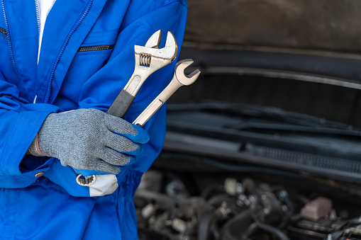 Close up hands of a male car mechanic holding a fix and an adjustable wranches with car engine in the background