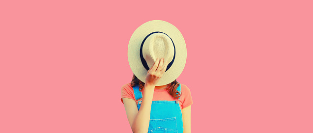 Portrait of unknown stranger young woman covering her face with summer straw round hat on pink background