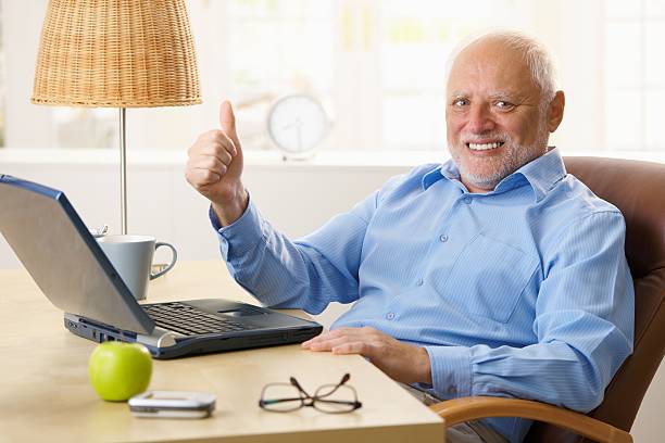 Happy senior man giving thumb up Happy senior man giving thumb up, sitting at desk using laptop computer at home... senior men stock pictures, royalty-free photos & images