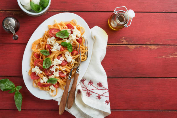 salat-caprese oder pasta-spaghetti gebrochen mit basilikum und mozzarella ala caprese auf einem weißen teller auf rotem rustikalem holzhintergrund. traditionelle italienische küche. italienisches food-konzept. draufsicht. - caprese salad antipasto wine mozzarella stock-fotos und bilder