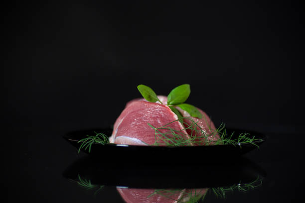 a piece of fresh pork meat in a plate, isolated on a black background.