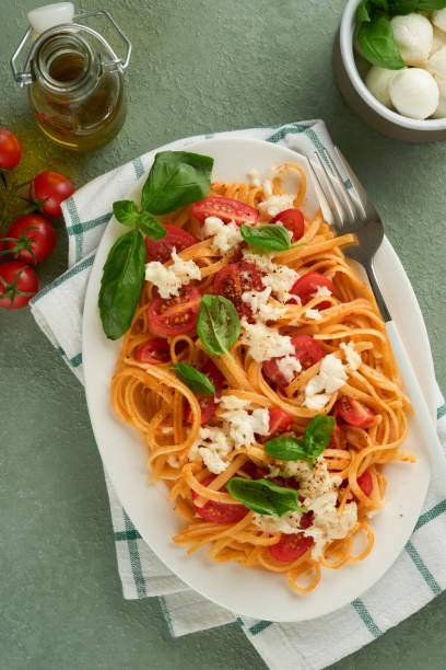 salat-caprese oder pasta-spaghetti gebrochen mit basilikum und mozzarella ala caprese auf weißem teller auf grünem rustikalem holzhintergrund. traditionelle italienische küche. italienisches food-konzept. draufsicht. rezept. - caprese salad antipasto wine mozzarella stock-fotos und bilder