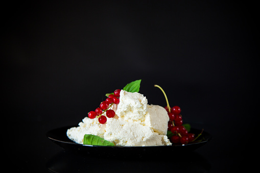 Natural homemade cottage cheese in a plate, isolated on a black background