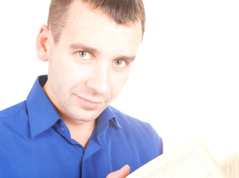 Serious student boy is reading a textbook sitting in the school classroom.