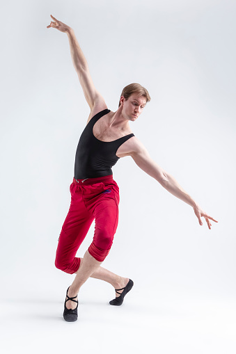 Concentrated Contemporary Ballet Dancer Flexible Athletic Man Posing in Red Tights in Ballanced Dance Pose With Hands In Line on White.Vertical Composition