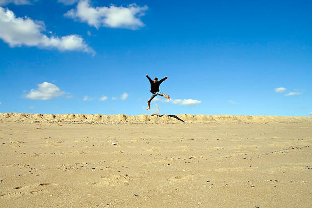 Young Man Jumping Off a Sand Ledge at the Beach stock photo