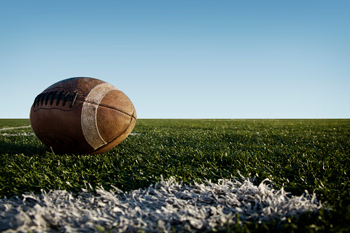 A used, worn football laying on a football field.