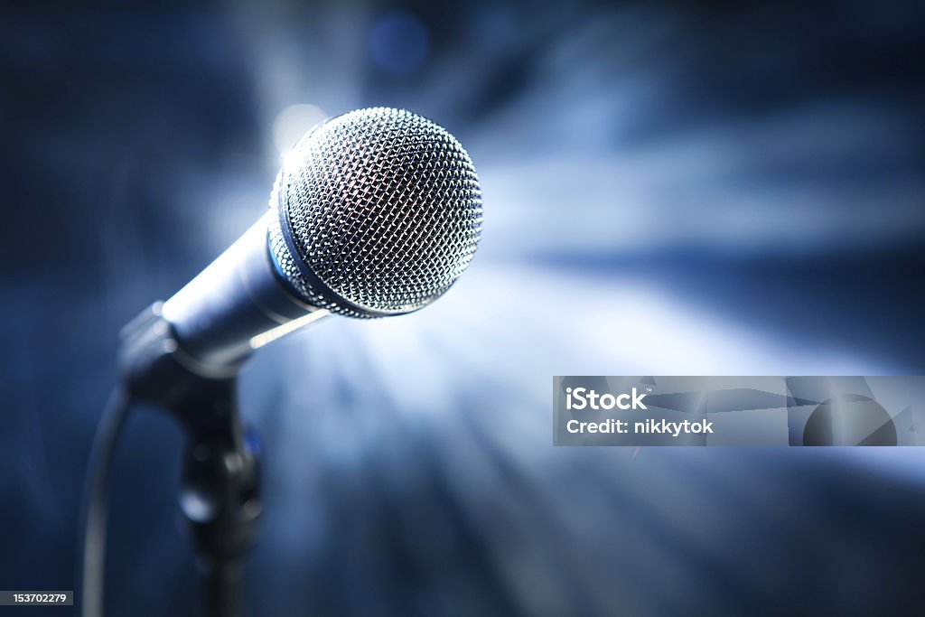 Microphone on stage Microphone on stage with blue shiny rays as the background Audio Equipment Stock Photo