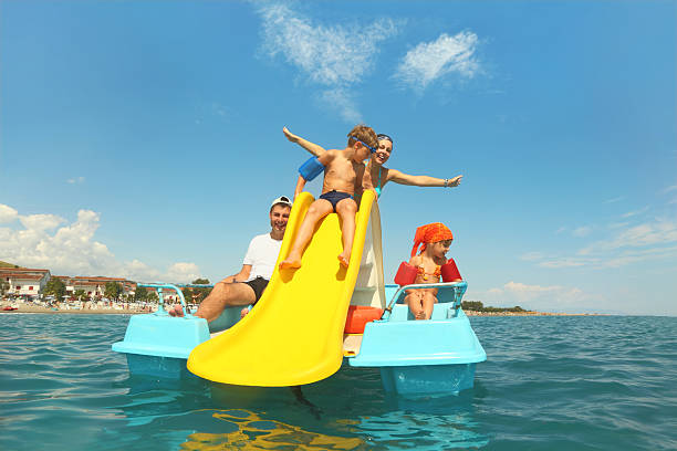 Family with boy and girl on pedal boat in sea Family with boy and girl on pedal boat with yellow slide in sea, view from water, shot from waterproof case paddleboat stock pictures, royalty-free photos & images