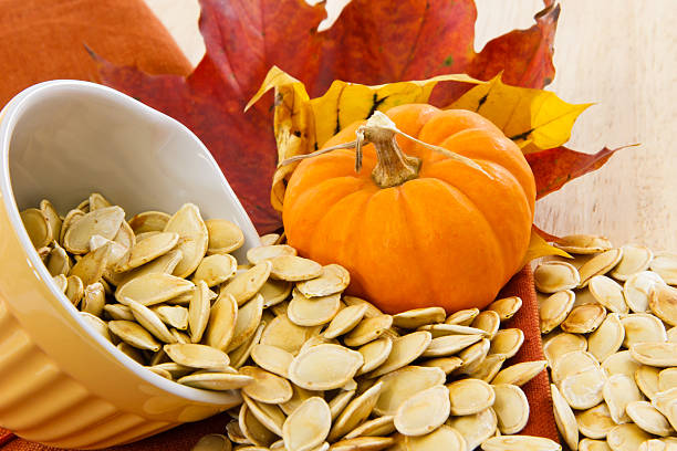 tostado semillas de calabaza amarilla derramando desde un recipiente amarillo - pepita de calabaza fotografías e imágenes de stock