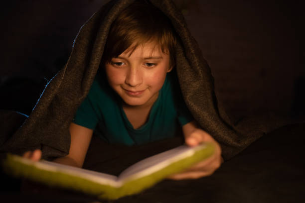 istock a child under a blanket in the dark reads a book instead of sleeping while no one sees it 1537052198