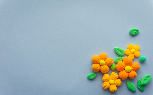Airy orange flowers with green leaves made of light plasticine, a background with space for your text. Eco theme, plants and gardening.