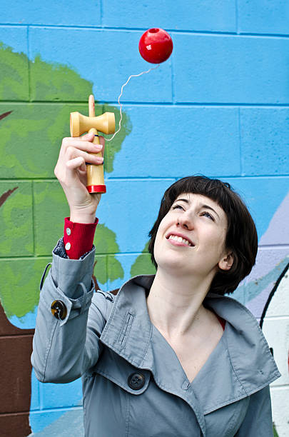 Young woman playing with traditional Japanese kendama Young woman in grey coat playing with traditional Japanese kendama kendama traditional japanese toy stock pictures, royalty-free photos & images