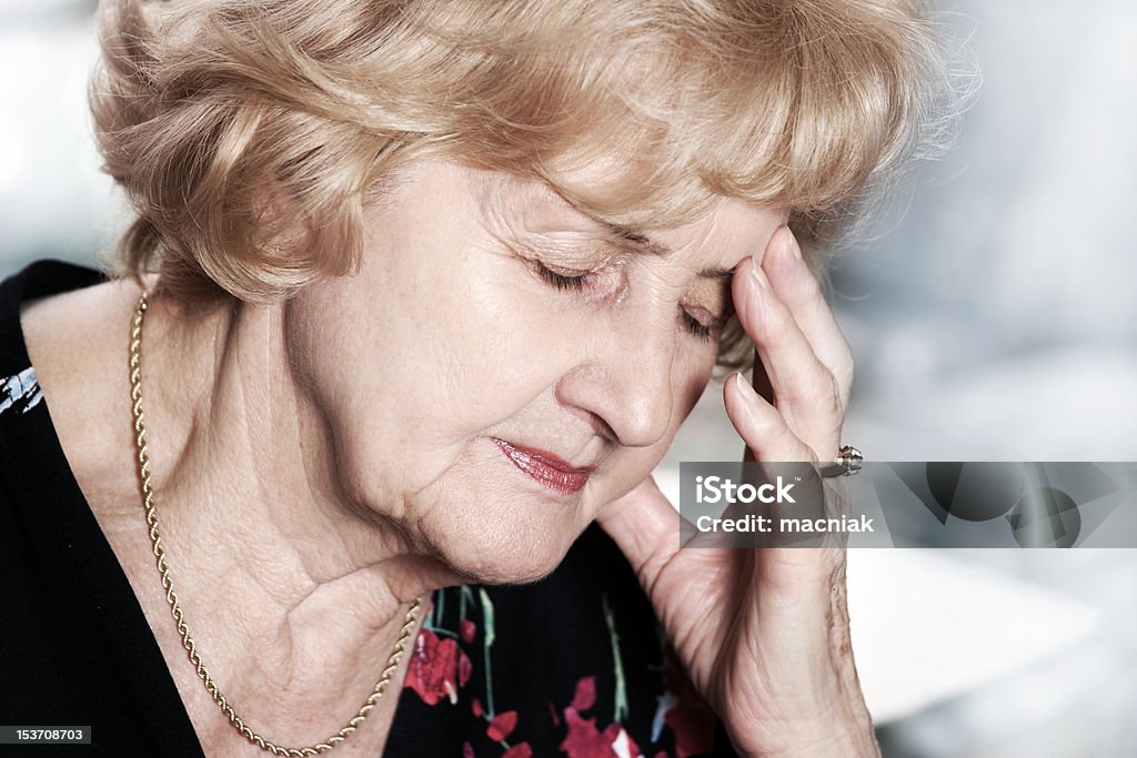 Senior lady with headache A portrait of a senior lady having headache over dark background Adult Stock Photo