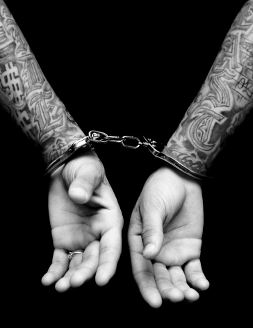 Tattooed male with hands behind his back and handcuffs on