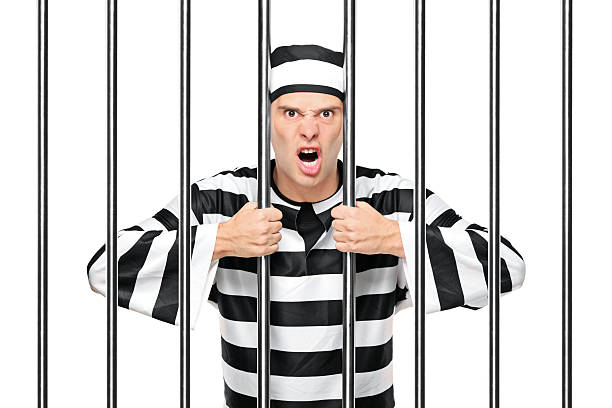 An agitated prisoner in jail holding bars isolated on white background