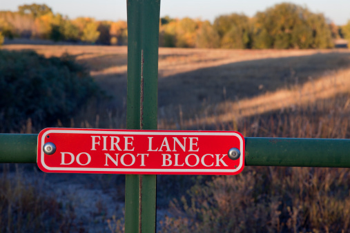 fire lane, do not block sign on a gate with a meadow and woods landscape behind