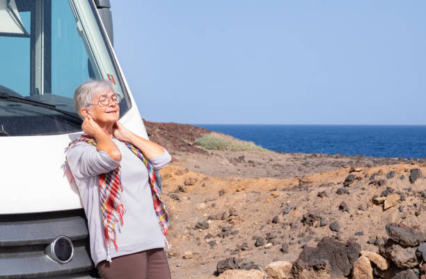 행복한 은퇴한 노인들은 야외에서 캠핑카를 타고 바다 가까이에 주차되어 무료 휴가와 여행을 즐기고 있다. 할머니는 얼굴에 태양을 느낀다 - image alternative energy canary islands color image 뉴스 사진 이미지