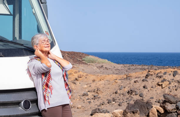 mulher sênior aposentada feliz ao ar livre seu veículo de van campista estacionado perto do mar desfrutando de férias gratuitas e viagens. senhora idosa sentir o sol em seu rosto - image alternative energy canary islands color image - fotografias e filmes do acervo