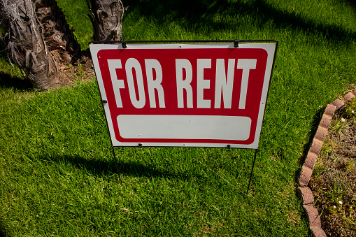 A red For Rent sign on a lawn in front of a house