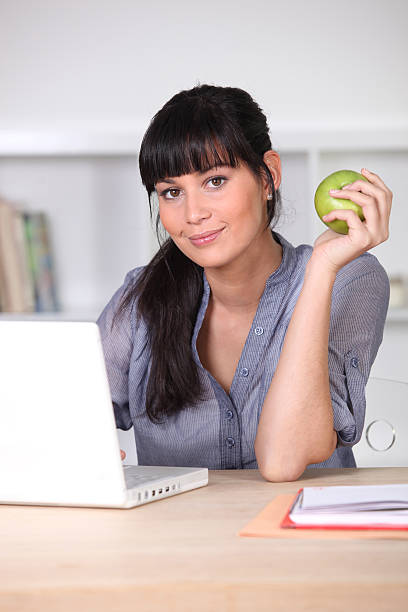 Young woman with apple in front of laptop computer