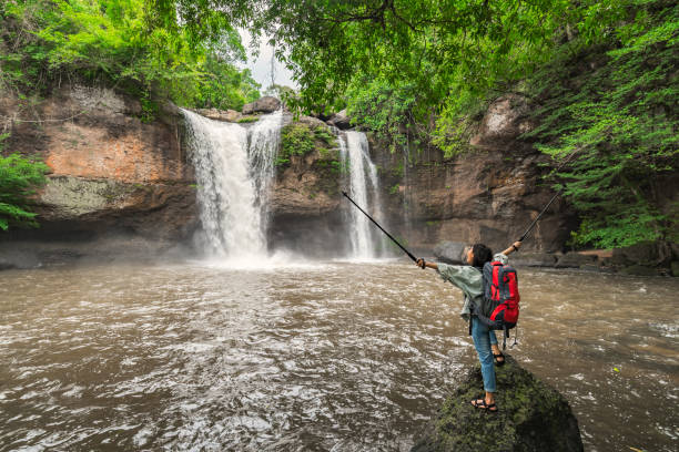 asian female tourists, trekking, experience the atmosphere of haew suwat waterfall in tropical forest. khao yai national park, thailand. young asian woman trekking to see waterfall in middle of forest - travel travel locations nature erawan imagens e fotografias de stock
