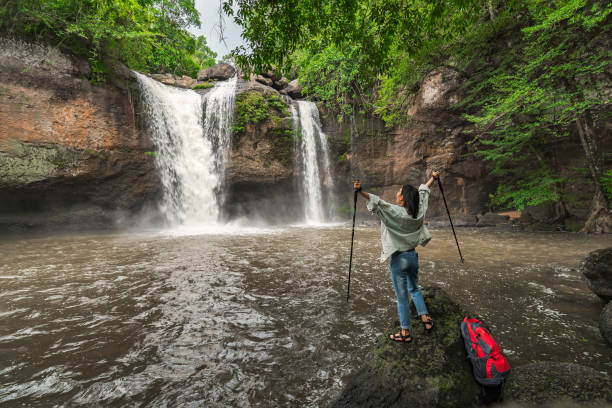 asian female tourists, trekking, experience the atmosphere of haew suwat waterfall in tropical forest. khao yai national park, thailand. young asian woman trekking to see waterfall in middle of forest - travel travel locations nature erawan imagens e fotografias de stock