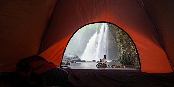 Asian female tourists camping in a cave in the middle of the forest To experience the atmosphere of a waterfall in tropical forest area of Thailand. Asian woman camping to see a beautiful waterfall.