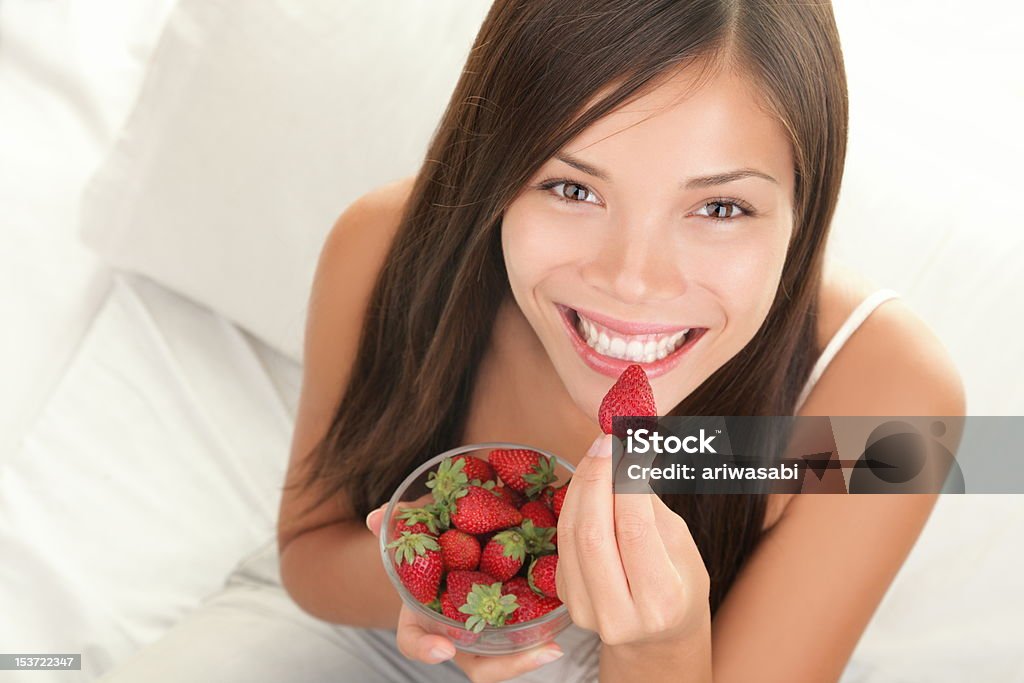 Strawberries woman Portrait of woman eating strawberries. Healthy happy smiling woman eating strawberry inside in bed holding a bowl of strawberries. Gorgeous smile on mixed Caucasian Asian female model. See more: Eating Stock Photo